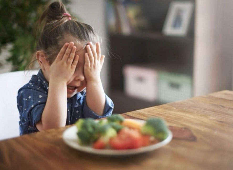 Criança recusando vegetais na mesa de jantar