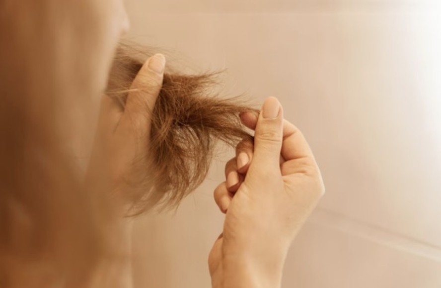 Mulher observando fios de cabelo na mão, simbolizando preocupação com queda capilar